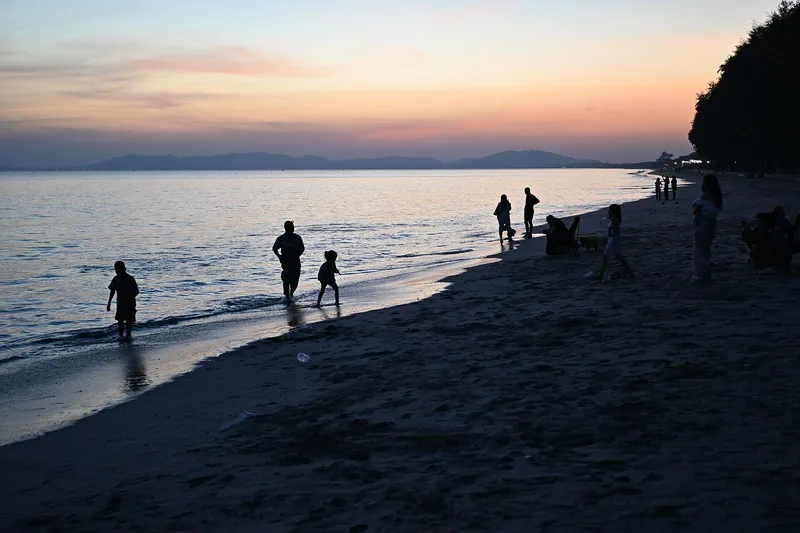 Silhouettes d'une famille marchant au bord de l'eau au coucher du soleil